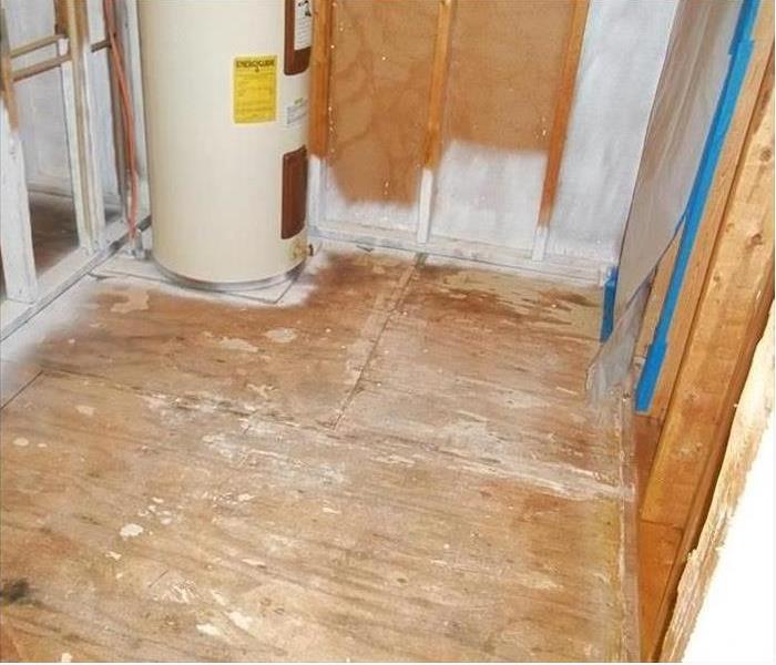 stripped down to studs and plywood floor, water heater in room