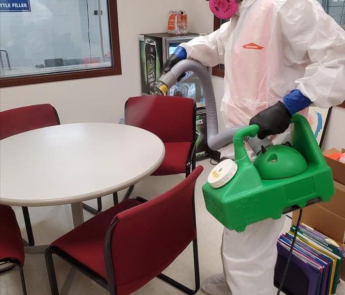 A SERVPRO employee with a white suit on spraying a table. 