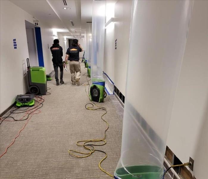 Hallway with  some demolition, air movers and plastic tubing forcing air into ceiling cavities, and nearby SERVPRO drying equ