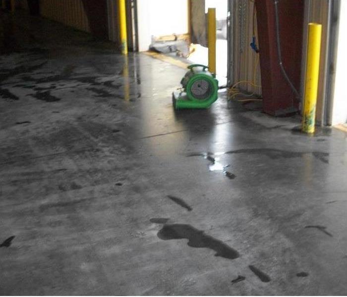 green air mover, small puddle of water, three yellow collision poles in a bay door extrance